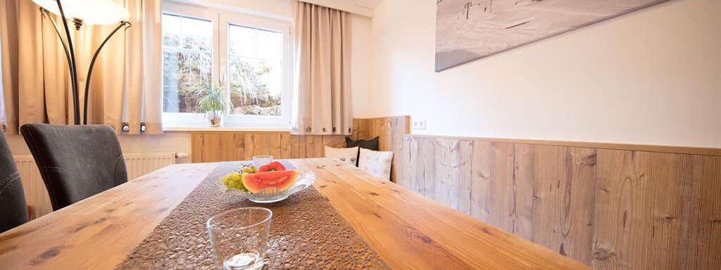 A cozy dining area with a large wooden table and modern chairs. The window lets in light and offers a beautiful view outside. - Haus Gondelblick - Sölden