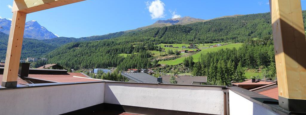A sunny terrace with a wooden roof offers a beautiful view of the green mountains. The landscape is picturesque and invites relaxation. - Haus Gondelblick - Sölden