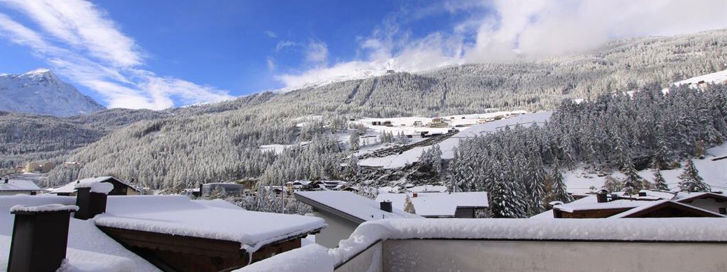 A snow-covered mountain landscape under a blue sky. The roofs of the houses are also covered with snow. - Haus Gondelblick - Sölden