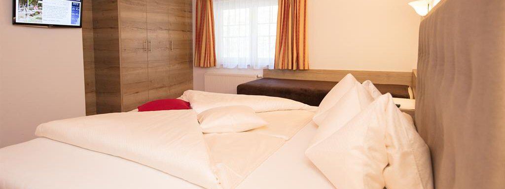 A cozy bedroom with a large bed and soft pillows. The wooden beam ceiling and daylight create an inviting atmosphere. - Haus Gondelblick - Sölden