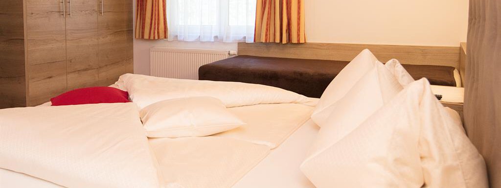 A cozy bedroom with a large bed and many pillows. The room has warm lighting and simple furniture. - Haus Gondelblick - Sölden