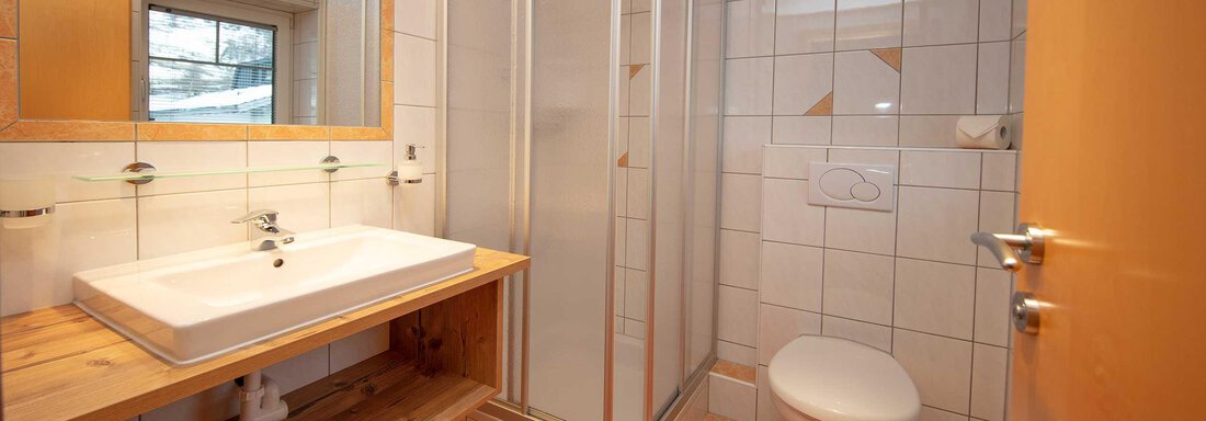 A modern bathroom with a shower, a sink, and a toilet. The walls are tiled and there is plenty of natural light coming through the window. - Haus Gondelblick - Sölden