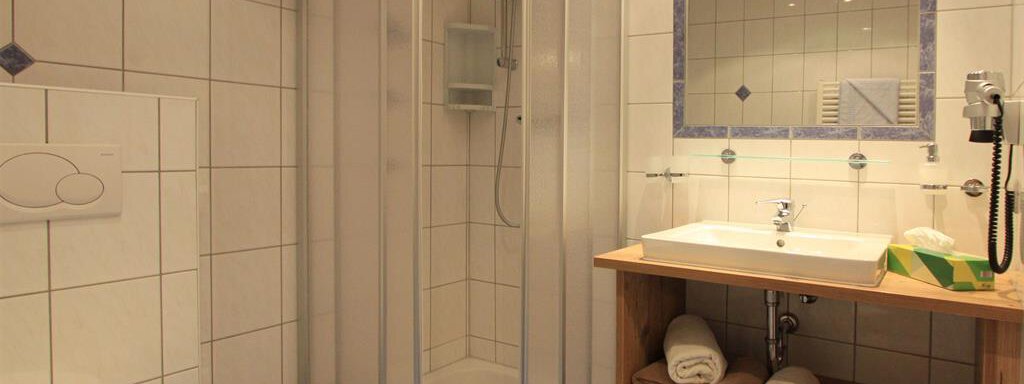 A modern bathroom with a wooden shower and sink. The walls are tiled, and there are fresh towels on a shelf. - Haus Gondelblick - Sölden