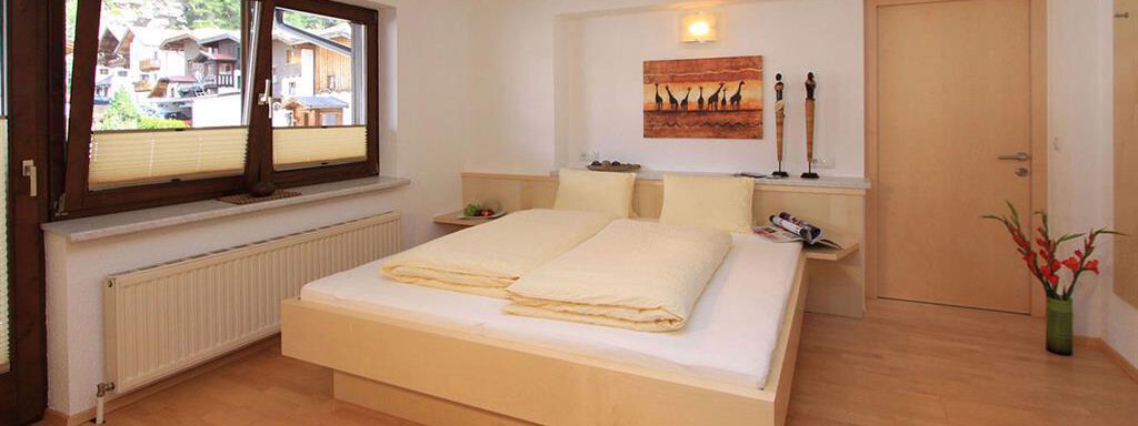 A bright bedroom with a large bed and built-in furniture. Large windows offer a view outside and provide plenty of daylight. - Haus Ingrid - Sölden