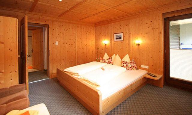 A cozy room with wooden paneling and a double bed. There is also a seating area and access to a balcony. - Haus Ingrid - Sölden