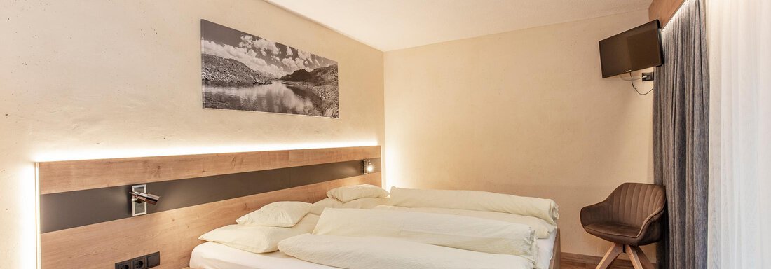 A modern bedroom with a double bed and bright wood design. A picture of a landscape hangs on the wall, and there is a comfortable chair and a window with curtains. - Haus Manfred - Sölden