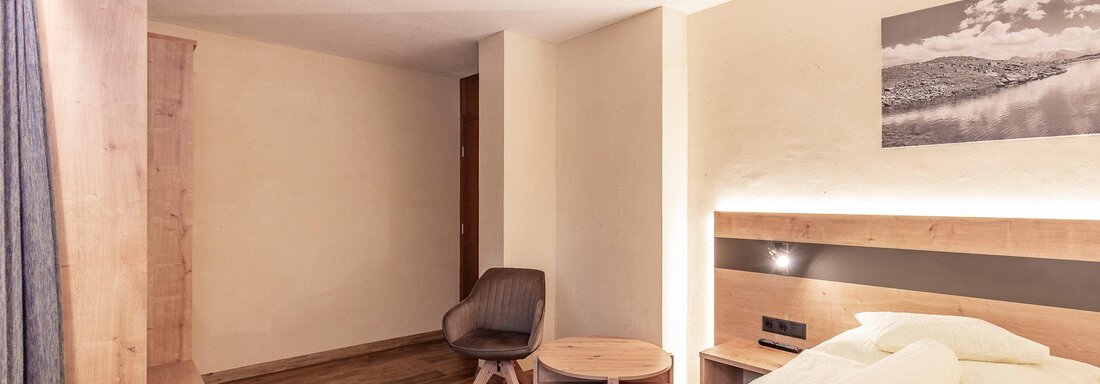 A modern hotel room with a single bed, a chair, and a small table. The walls are light and the floor is made of wood. - Haus Manfred - Sölden