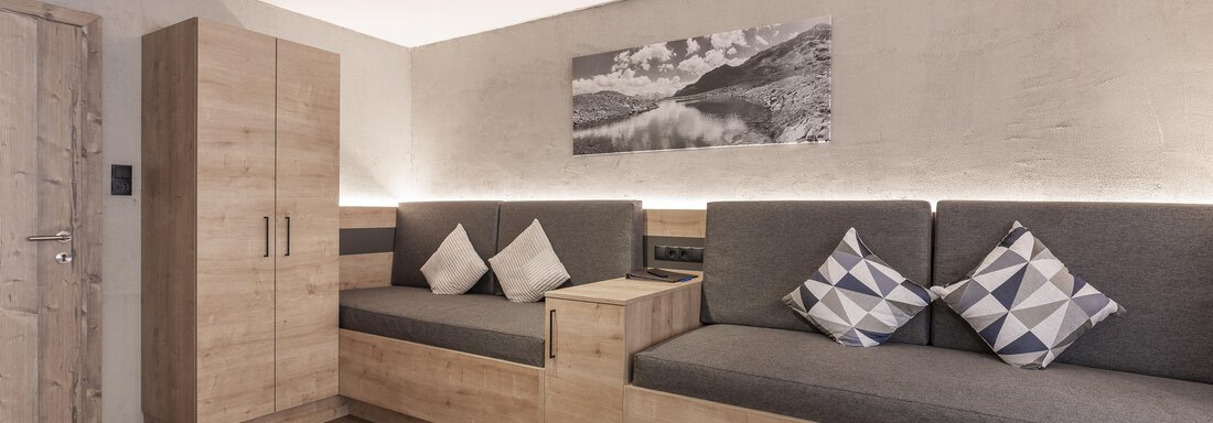 A modern living space with cozy seating and cushions. The walls are painted in neutral tones and there are wooden details. - Haus Manfred - Sölden