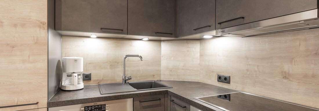 A modern kitchen with dark cabinets and a bright countertop. The equipment includes a sink, a dishwasher, and a cooktop. - Haus Manfred - Sölden