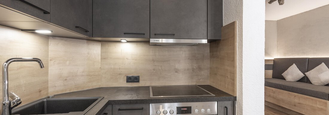 A modern kitchen unit with black cabinets and stainless steel appliances. The space feels bright and inviting with wooden elements. - Haus Manfred - Sölden