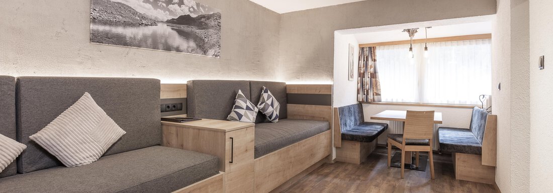 A modern living room with cozy seating in gray and wood. There is a dining area with a table and chairs, as well as plenty of natural light. - Haus Manfred - Sölden