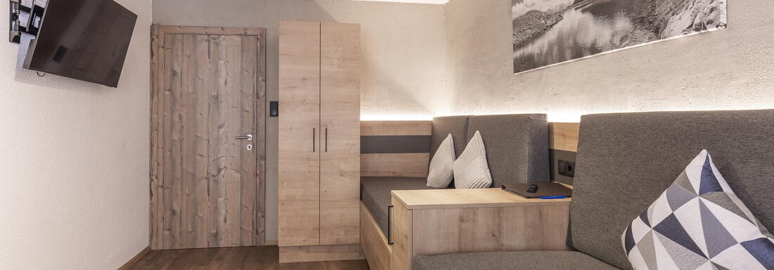 A modern room with wooden flooring and cozy seating. On the wall hangs a television and a large photo of a scenic motif. - Haus Manfred - Sölden