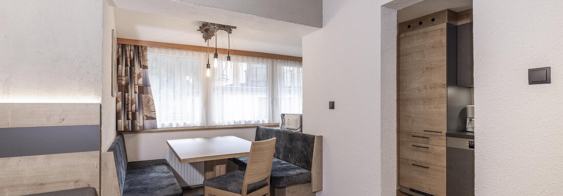 A modern apartment with a cozy dining area and a kitchenette. Bright walls and wooden floors create an inviting atmosphere. - Haus Manfred - Sölden