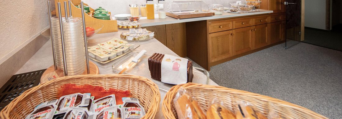 A hearty breakfast buffet with various rolls and spreads. In the background, glasses and a counter are visible. - Haus Montjola - Sölden