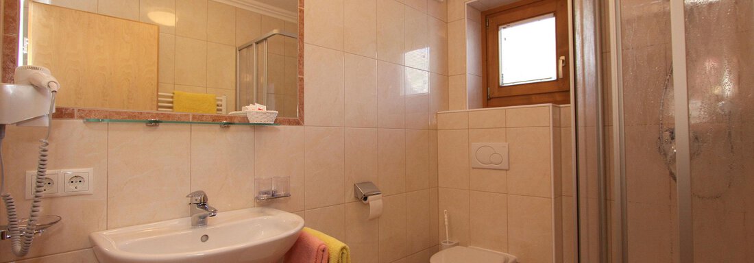 A modern bathroom with a shower, a sink, and a toilet. The walls are brightly tiled and a large mirror is located above the sink. - Haus Montjola - Sölden