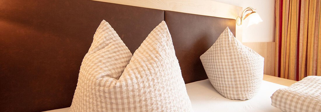 Beispiel Doppelzimmer A cozy bedroom with two large, striped pillows. The warm colors and simple design create a relaxed atmosphere. - Haus Montjola - Sölden