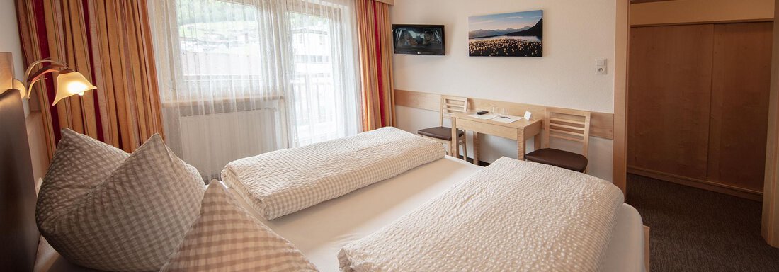 A cozy hotel room with two single beds and large windows. It features a pleasant decor with bright colors and a small table with chairs. - Haus Montjola - Sölden