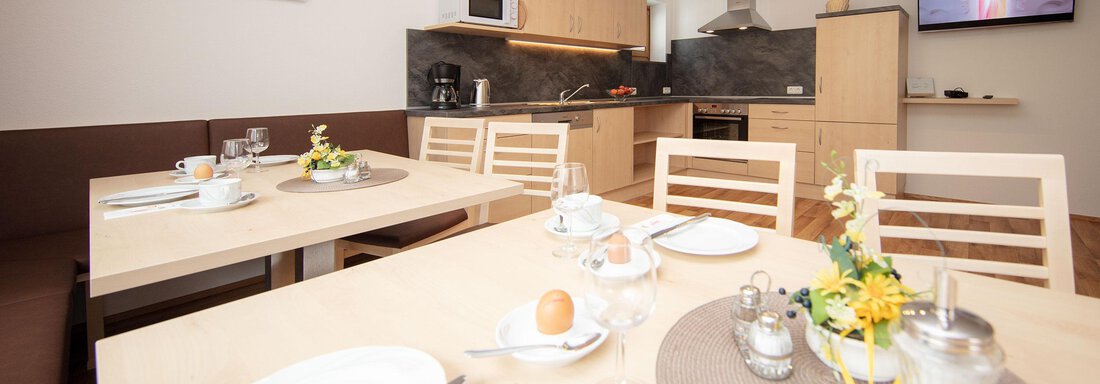 A modern kitchenette with bright wooden furniture. The table is set for breakfast, with dishes and decorative flowers. - Haus Montjola - Sölden
