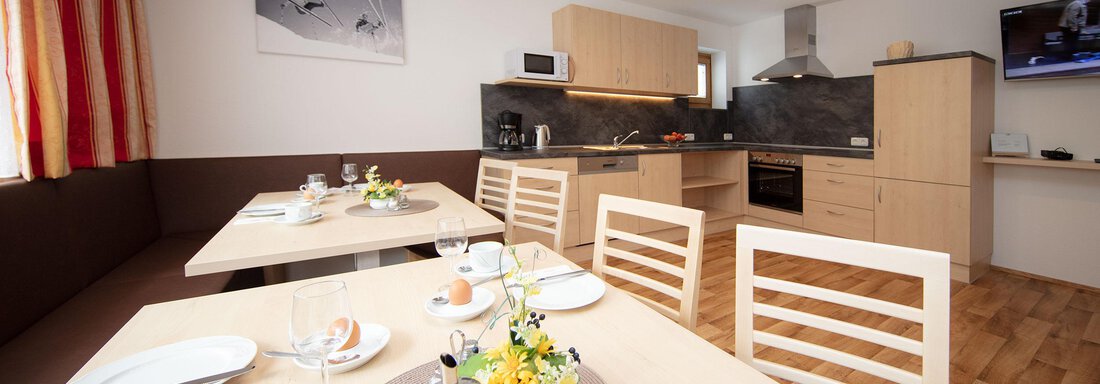 A modern kitchen with a dining area and light wooden furniture. The table is set with dishes and fresh flowers. - Haus Montjola - Sölden