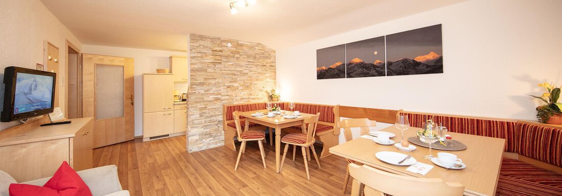 A modern living room with wooden flooring and a cozy dining area. The space is bright and welcoming, with a television and beautiful wall decoration. - Haus Montjola - Sölden