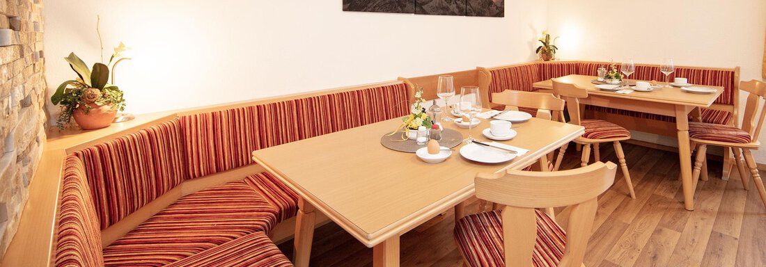 A cozy dining area with wooden chairs and a large table. The walls are bright, and decorated plates and flowers are on the table. - Haus Montjola - Sölden