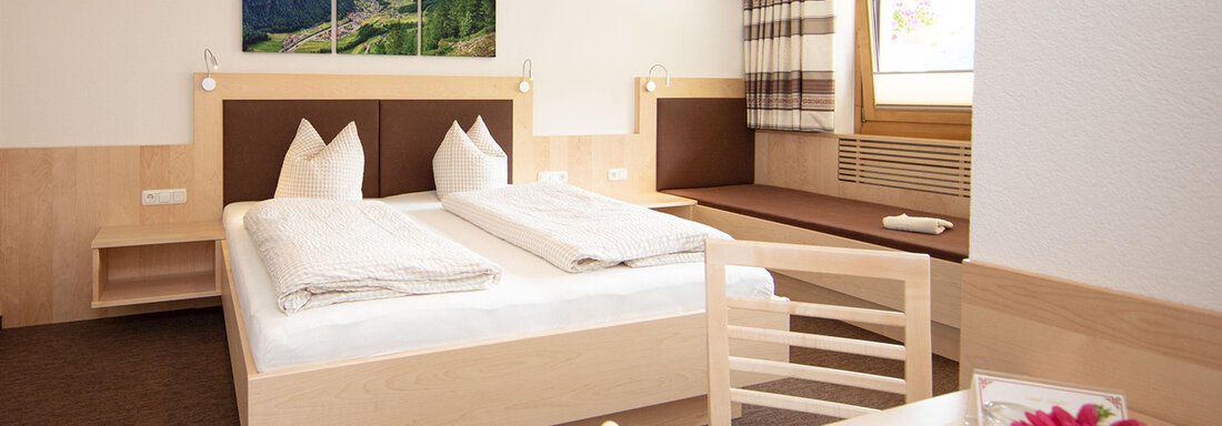 A modern hotel room with two single beds and soft wood tones. The room is brightly lit and offers a cozy seating area as well as a window with a view. - Haus Montjola - Sölden