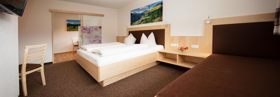 A modern bedroom with a double bed and an additional room with a single bed. The walls are light and a television is mounted on the wall. - Haus Montjola - Sölden