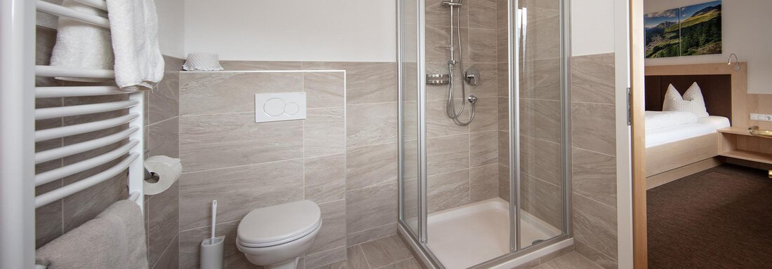 A modern bathroom with a shower, a toilet, and a towel holder. The room is bright and designed in neutral colors. - Haus Montjola - Sölden