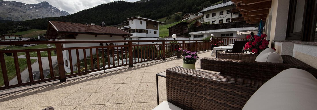 A cozy terrace with a view of the mountains and surrounding houses. Comfortable furniture and blooming plants create an inviting atmosphere. - Haus Montjola - Sölden