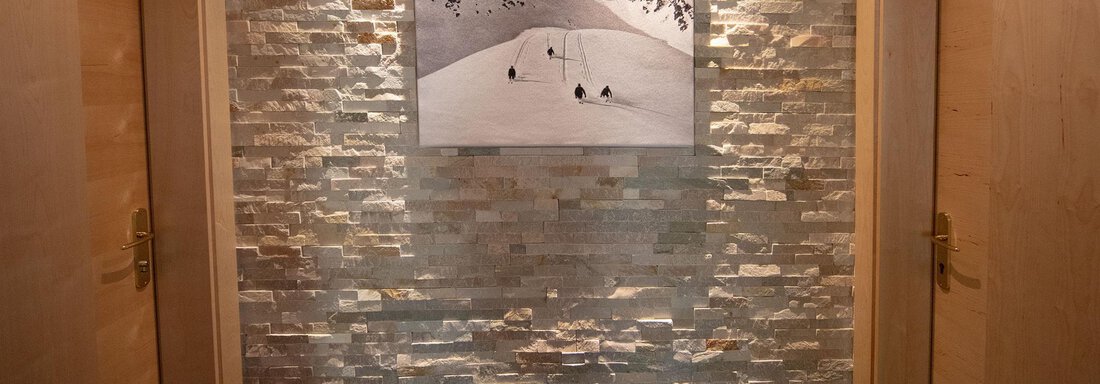 A plain corridor with two wooden doors and a stone wall. On the wall hangs a picture of snow-covered mountains. - Haus Montjola - Sölden