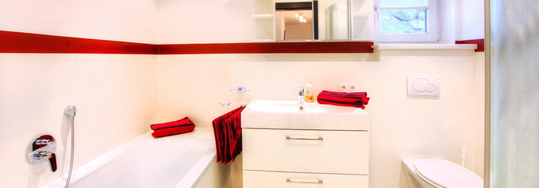A modern bathroom with a bathtub and a white dresser. Red towels and an elegant wall decoration provide a color accent. - Haus PIA by A CASA - Sölden