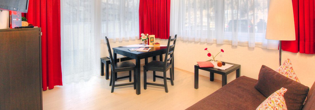 A cozy living room with a sofa and a dining table. Red curtains create a warm atmosphere. - Haus PIA by A CASA - Sölden