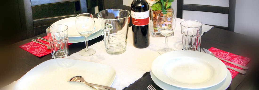 An elegant covered table with a white tablecloth, red wine, glasses, and flowers. The plates are set for a festive meal. - Haus PIA by A CASA - Sölden