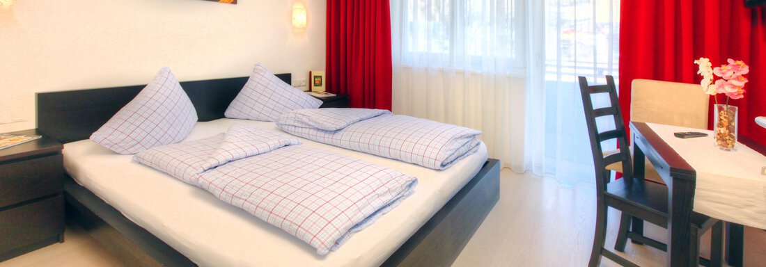 A modern bedroom with a large double bed and bright wooden floors. Red curtains and a desk create a cozy atmosphere. - Haus PIA by A CASA - Sölden