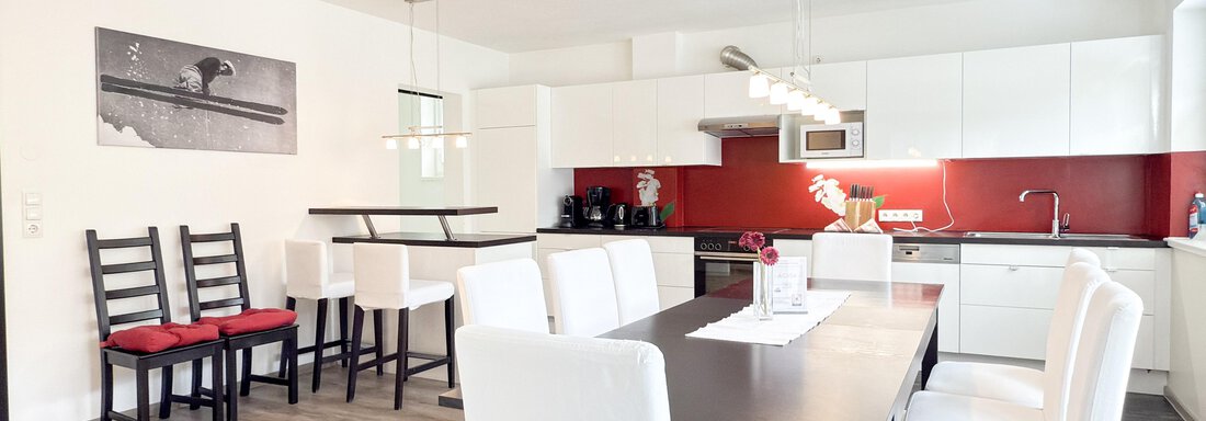 HAUS PIA IMG_3683 A modern kitchen with a large table and white chairs. The walls are red and there is stylish lighting. - Haus PIA by A CASA - Sölden