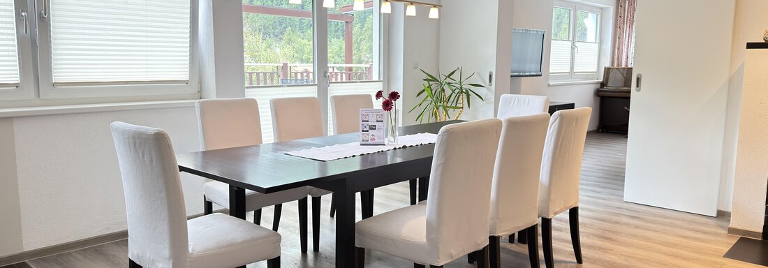 A modern dining area with a large table and eight white chairs. Windows let in plenty of light, and a plant adds a friendly atmosphere. - Haus PIA by A CASA - Sölden