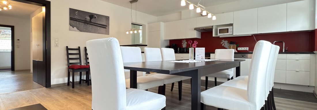 A modern dining room with a large table and white chairs. The kitchen is open and has red accents as well as modern appliances. - Haus PIA by A CASA - Sölden