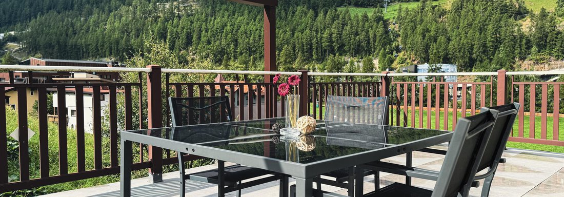 A stylish table with chairs on a terrace, surrounded by green mountains. The clear sky and nature provide a relaxing atmosphere. - Haus PIA by A CASA - Sölden