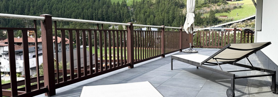 A balcony with a chaise lounge and a parasol. In the background, green hills and small houses can be seen. - Haus PIA by A CASA - Sölden