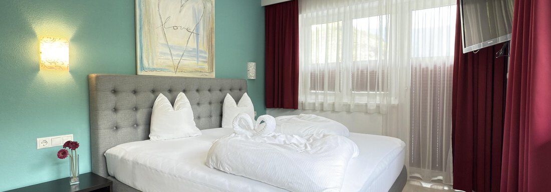 A modern bedroom with a large bed and fresh white towels. The walls are painted in a soothing green tone, and large windows let in plenty of light. - Haus PIA by A CASA - Sölden