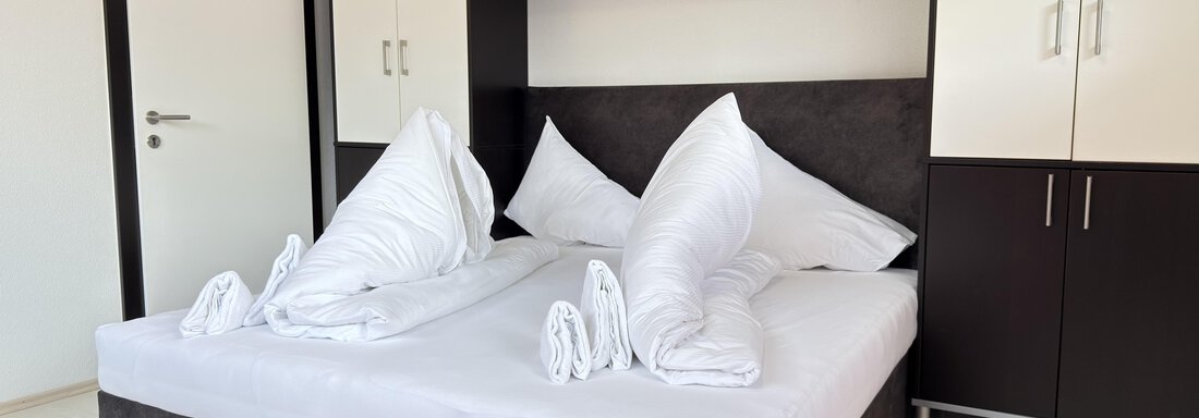 A modern bedroom with a large bed and white bedding. The furniture is in black and white, with plenty of storage space. - Haus PIA by A CASA - Sölden