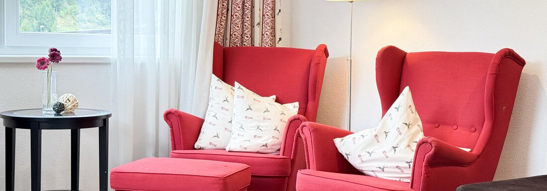 Two red armchairs with cushions are in a bright living room. Next to them, there is a small table and a lamp light shines softly. - Haus PIA by A CASA - Sölden
