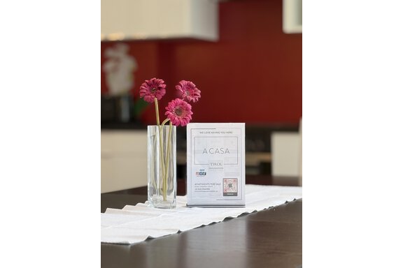 An elegant table with a transparent vase containing pink flowers. Next to the vase is an information sheet about a stylishly designed house. - Haus PIA by A CASA - Sölden