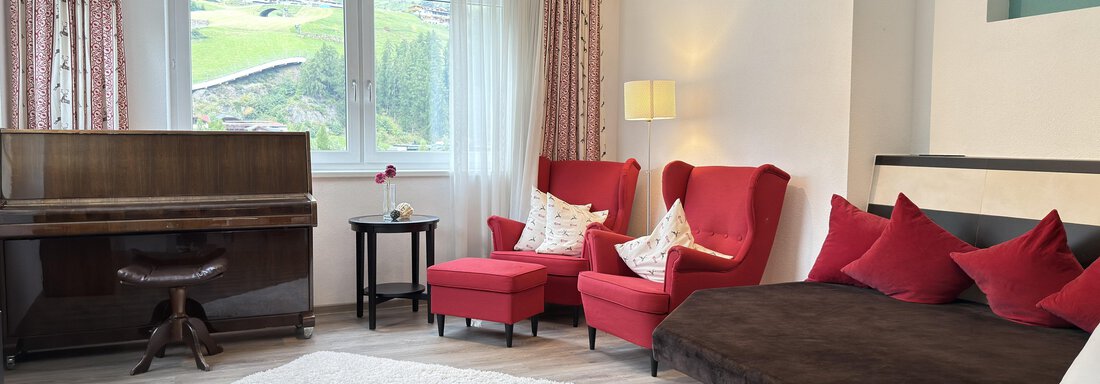 A stylish living room with red armchairs and a piano. The room is bright and cozy, with a large window that offers a beautiful view. - Haus PIA by A CASA - Sölden