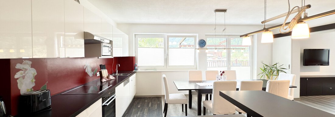 A modern kitchen with white cabinets and a dark countertop. The dining area is bright and inviting, featuring a table and chairs. - Haus PIA by A CASA - Sölden