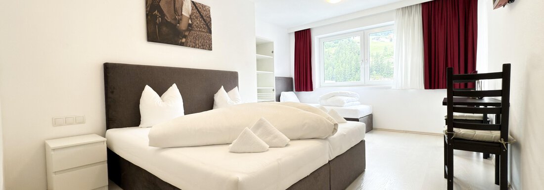 A modern room with a large double bed and two single beds. The room has bright walls and large windows that provide a lot of light. - Haus PIA by A CASA - Sölden
