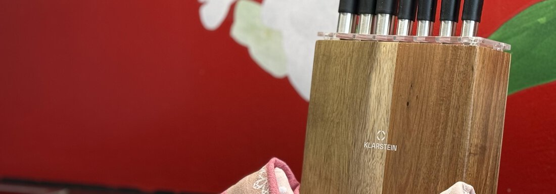 A wooden knife block with several sharp knives stands on a table. In the background, there are red walls with a blooming plant visible. - Haus PIA by A CASA - Sölden
