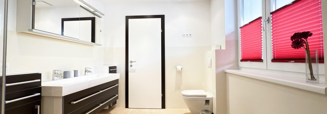 A modern bathroom with a large mirror and stylish furniture. The red window shutters add a color accent in the bright room. - Haus PIA by A CASA - Sölden