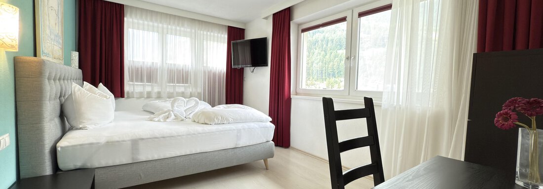 A modern hotel room with a large bed and a desk. Bright windows let in plenty of daylight. - Haus PIA by A CASA - Sölden