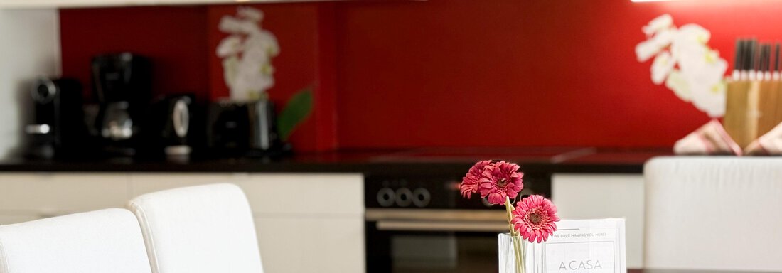 A modern kitchen with red walls and white furniture. On the table, there is a vase with pink flowers. - Haus PIA by A CASA - Sölden